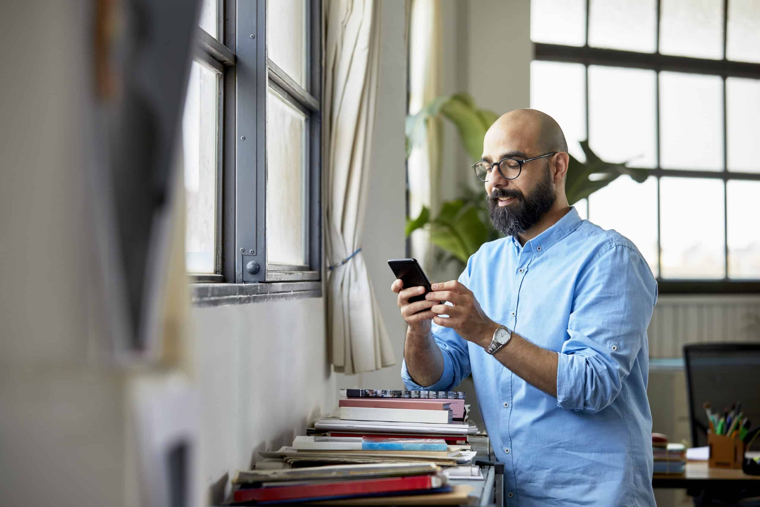 Man standing at a window, looking at his phone