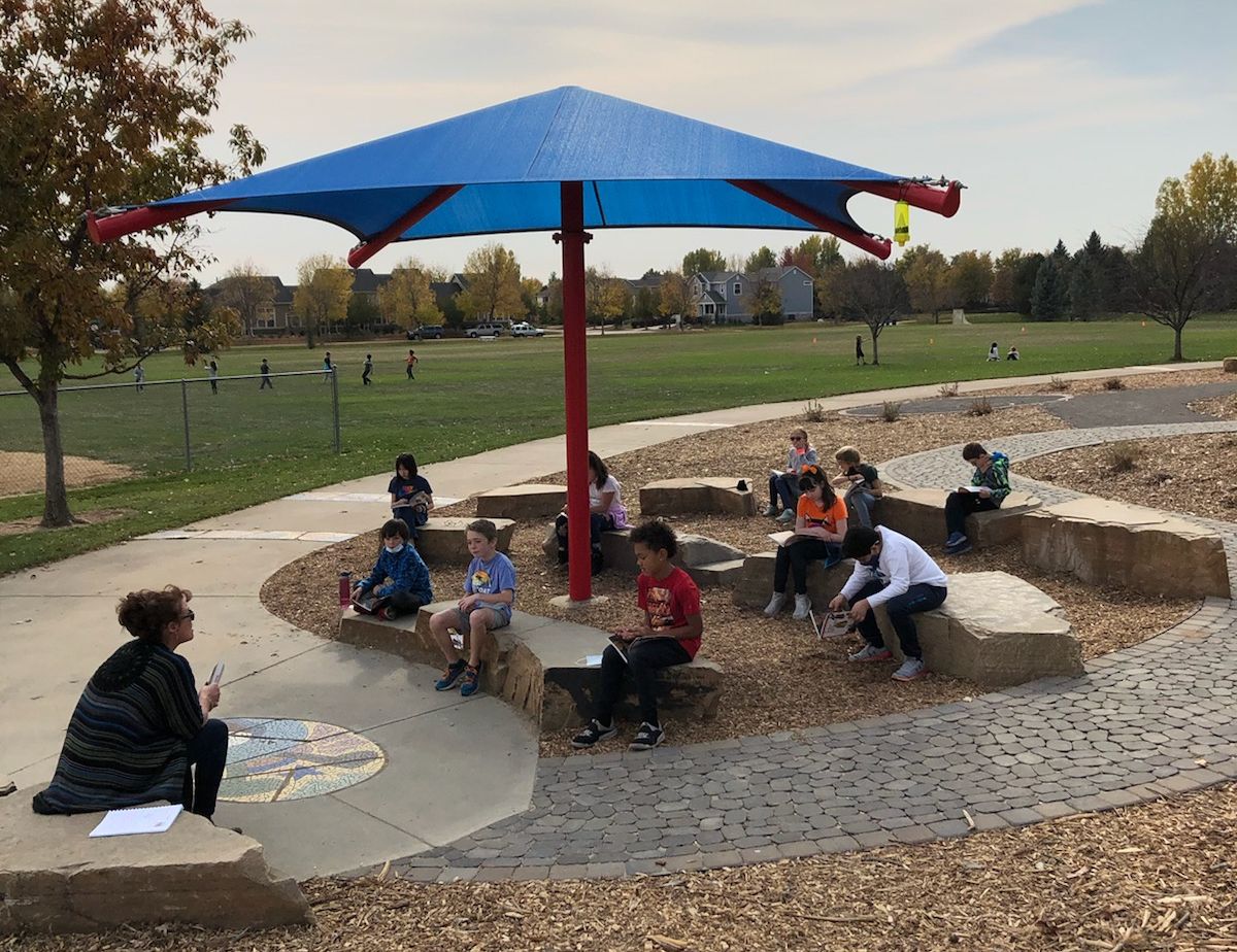 kids beneath an umberlla at picnic table in an outdoor class