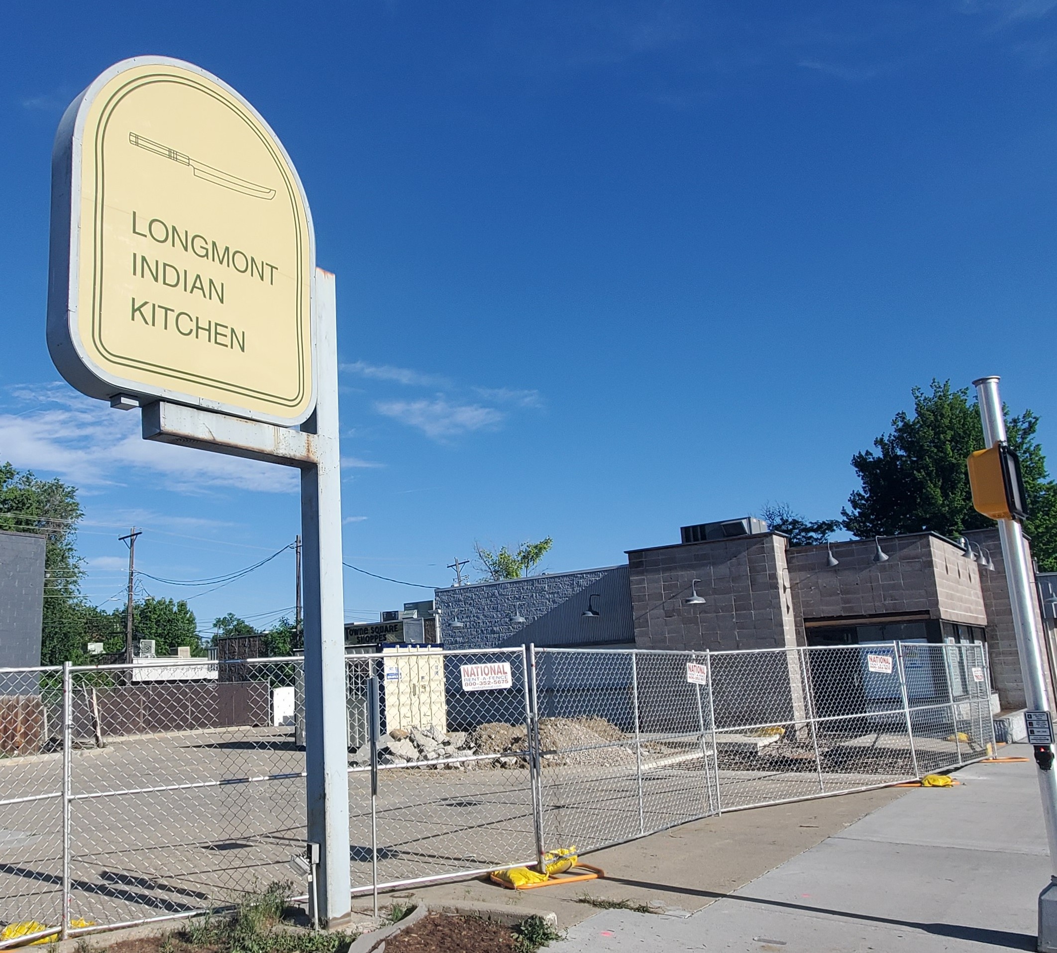 A sign at the southeast corner of Ninth Avenue and Coffman Street heralds the upcoming opening of Longmont Indian Kitchen as construction work continues on its building.