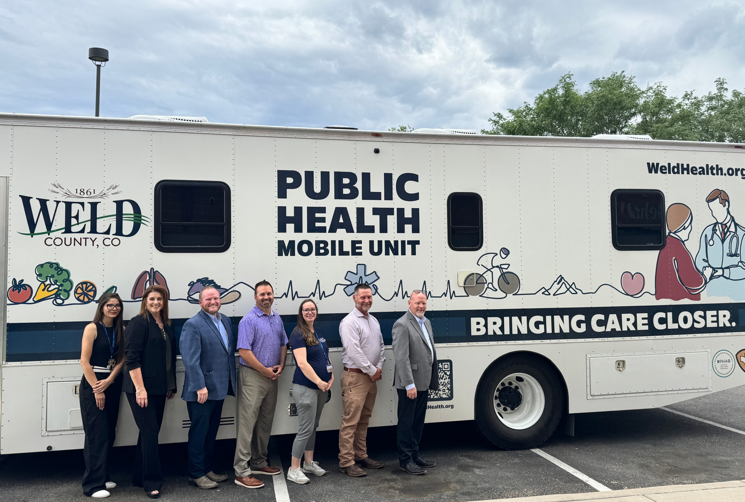 Standing next to a Weld County Public Health mobile unit are, from left: Shanti Sanchez, public health services outreach coordinator, Weld County Department of Public Health and Environment; Kim Collins, CEO, North Range Behavioral Health; Shaun May, public health services director, WCDPHE; Kyle Holman, director of health grants, The Weld Trust; Olivia Egen, community health director, WCDPHE; Jason Chessher, executive director, WCDPHE; and Jeff Carlson, CEO, The Weld Trust.